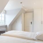 Schlafzimmer mit Dachschrägen, weißem Bett, Kleiderschrank und Fenster.