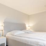 Schlafzimmer mit Doppelbett, Nachttisch und Wandfernseher.
