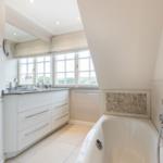 Badezimmer mit Badewanne, Waschbecken und Fenstern.