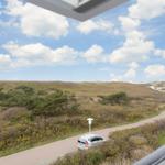 Dachterrasse mit Blick auf grüne Hügel und einen gepflasterten Weg mit einem weißen Auto.