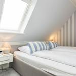 Schlafzimmer mit Dachfenster, gestreifter Wand und weißem Bett.