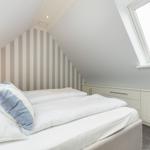 Schlafzimmer mit Dachschräge, gestreifter Wand und Dachfenster.
