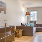 Wohnzimmer mit Sofa, Kissen, Schrank und Wandbild.