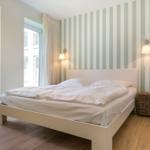 Schlafzimmer mit Bett, Streifenwand und Fenster.