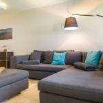 Ein Wohnzimmer mit grauem Sofa, blauen Kissen und einer Stehlampe.