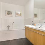 Badezimmer mit Badewanne, Waschbecken und Toilette. Wandbilder und Holzschränke.
