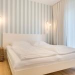 Schlafzimmer mit weißem Bett, gestreifter Wand und Holzboden.