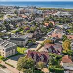 Aerial view of coastal town with houses, greenery, and ocean in background.