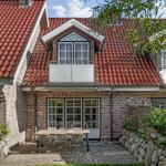 Haus mit rotem Dach, Terrasse und Gartenbereich mit Tisch und Stühlen.
