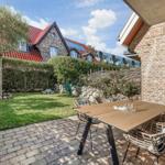 Terrasse mit Tisch und Stühlen, Grünfläche und Steinmauer im Hintergrund.