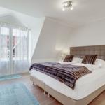 Schlafzimmer mit Doppelbett, blauer Sessel und Fenster zur Aussicht.