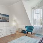 Schlafzimmer mit Dachschrägen, blauer Sessel und Fernseher an der Wand.