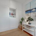 Wohnbereich mit weißen Schränken, Bonsai, Pflanze und Strandgemälde an der Wand.