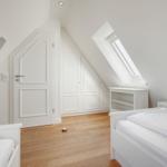 Zimmer mit zwei Betten, Dachschrägen, Fenster und Holzboden.