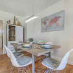Esszimmer mit Tisch, Stühlen und Wandbild. Hintergrund: Flur mit Tür.