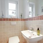 Bathroom with sink, toilet, and window. Wall cladding made of stone tiles.