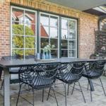 Terrace with table and chairs in front of brick house with windows.