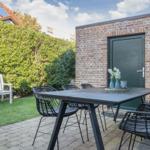 Outdoor area with table, chairs, and white garden bench against brick wall.