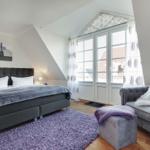 Bedroom with bed, sofa, and window. Wooden floor and purple rug.