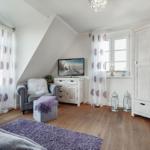 Bedroom with sloped ceiling, TV, gray armchair, and wooden floor.
