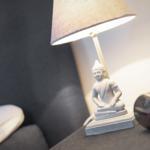 Table lamp with Buddha figurine on dark furniture piece.