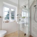 Bathroom with shower, sink, and toilet. Window with view of greenery.