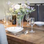 Wooden table with set places and flower vase in the middle.