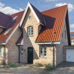 House with red tiled roof and brick facade, green doors and white garage door.