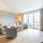 Living room with sofa, armchairs and wooden floor. Glass door leads to terrace.