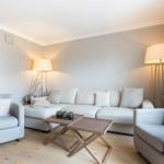 Living room with sofa, two armchairs, and wooden table. Lit by floor lamps.