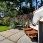 Outdoor area with lounger, table, and bottle of champagne. Background: grass, trees, and wooden wall.