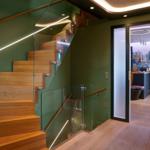 Wooden staircase with glass railing and green wall. Doorway to adjacent room.