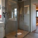 Shower with glass enclosure, sink, and mirror. Door leads to bedroom.