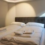 Double bed with white bedding and folded towels. Green nightstand with floor lamp.