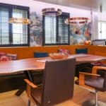 Dining area with wooden table, orange booth, and modern pendant lights.