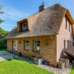 A thatched roof house with brick facade and garden area.