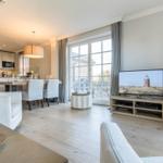 Living room with dining area and TV. Wooden floor and large windows.