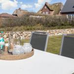 Outdoor area with table, chairs, and decorative items. Houses and stone wall are visible in the background.