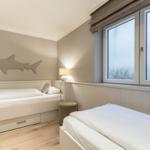 Room with two beds, shark wall decor, and sea view through window.