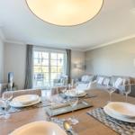 Dining room with table, glasses, and plates. Living area with sofa and window in background.