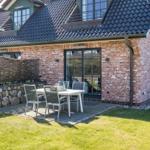 Terrace with table and chairs in front of a brick house with dark roof.