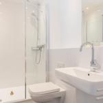 Badezimmer mit Dusche, Waschbecken und Toilette. Weiße Fliesen und Spiegel.