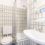 Badezimmer mit Dusche, Toilette und Waschbecken. Fliesen mit blauen Linien.