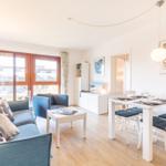 Wohn- und Essbereich mit Sofa, Tisch und Stühlen. Holzboden und Fenster.
