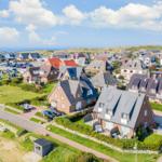 Houses with gardens and parking lots near the coast under blue sky.