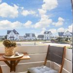 Balcony with chair and table, view of white houses and blue sky.
