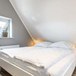 Bedroom with sloped ceiling, white bed, and window with plant.