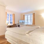 Bedroom with double bed, desk, and two windows with curtains.