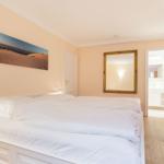 Bedroom with white bed, wall art, and view into the bathroom.