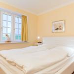 Bedroom with white bed, yellow walls, and window with yellow curtains.